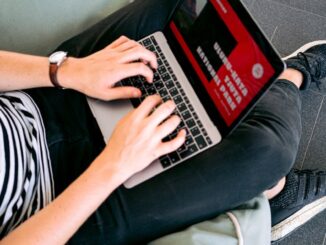 Une personne travaillant à distance sur un ordinateur portable tout en étant confortablement assise sur un pouf à l'intérieur.